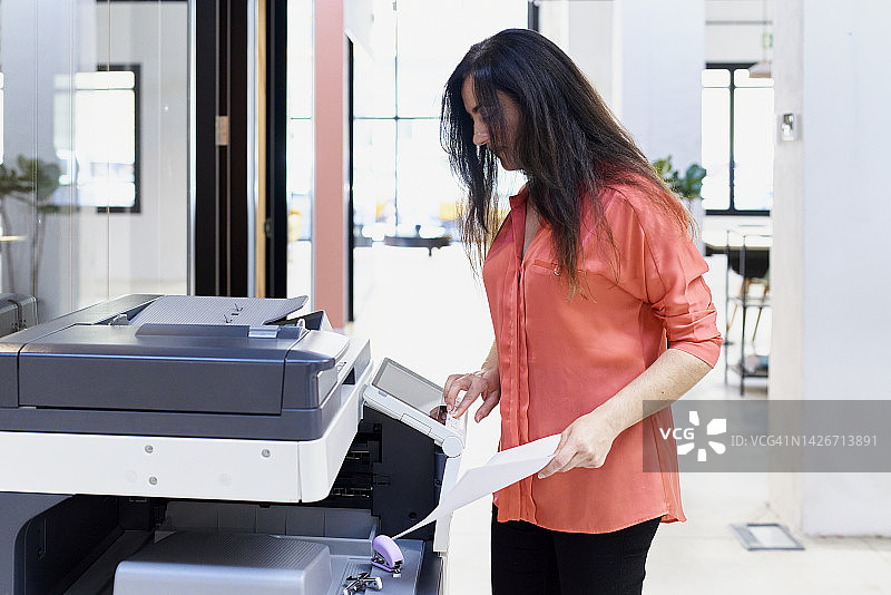 在现代办公室的会议室里，用复印机为员工会议复印报告的中年妇女图片素材