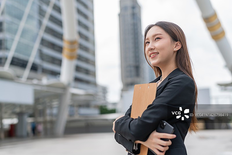 在曼谷中央商务区拿着文件夹和智能手机的亚洲女商人图片素材