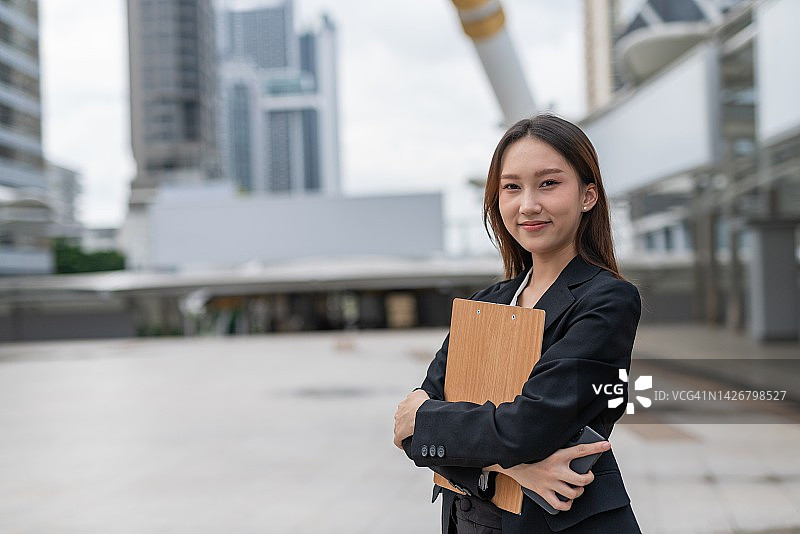 在曼谷中央商务区拿着文件夹和智能手机的亚洲女商人图片素材