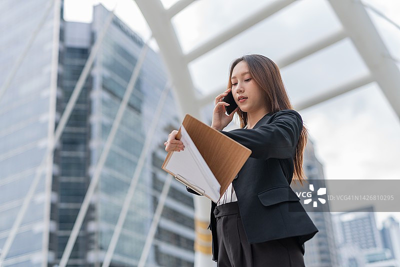 在曼谷中央商务区打电话看手表的亚洲女商人图片素材