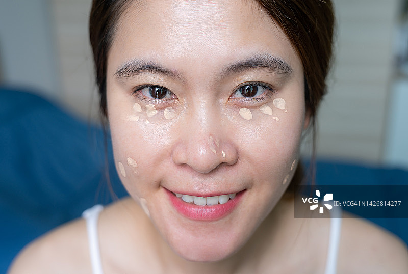 年轻的亚洲女人正在脸上涂抹遮瑕膏图片素材