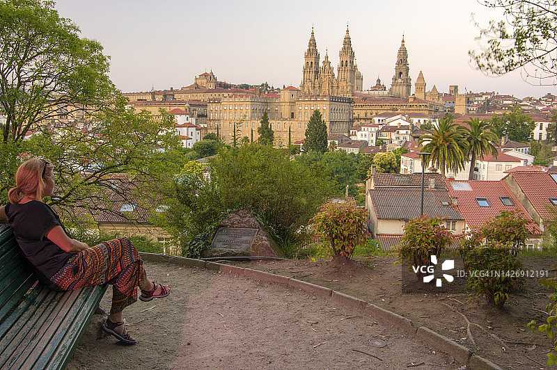 坐在长椅上眺望西班牙圣地亚哥·德孔波斯特拉大教堂的女人图片素材