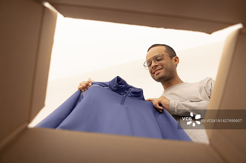 不同肤色人种的男人从送货上门的盒子里拿出他的新跑步服图片素材