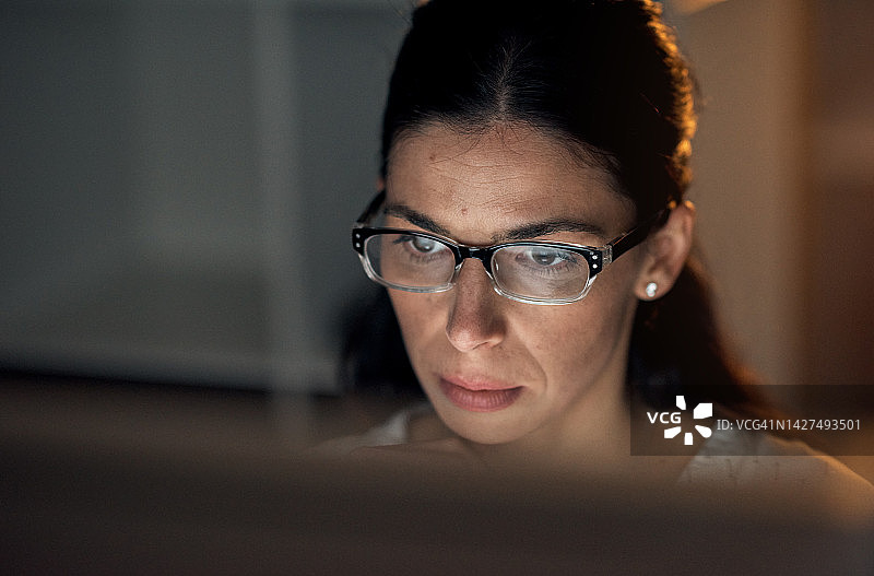 夜晚戴眼镜的商务女人用笔记本电脑进行在线研究图片素材
