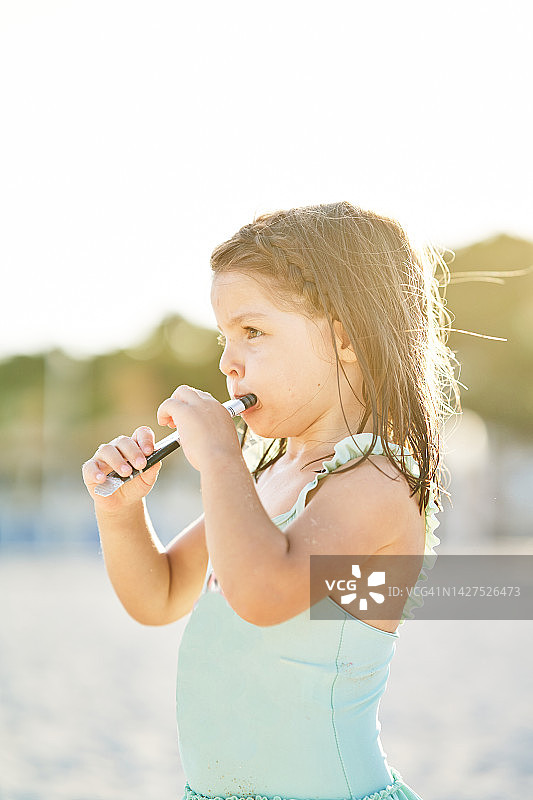 小女孩在海滩户外站着，看向远方，吃着冰淇淋图片素材