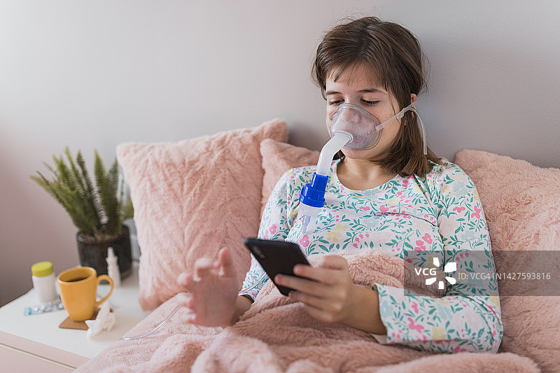 在家吸入药物时，女孩看着手机图片素材