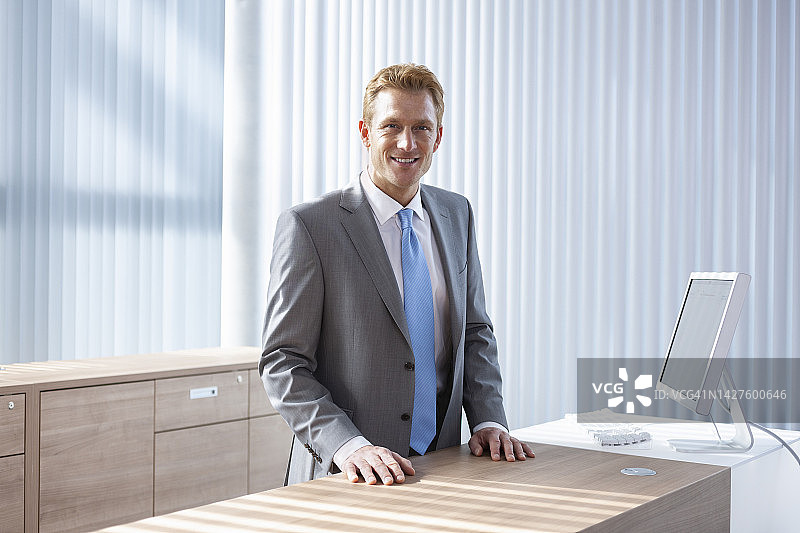 微笑的男商人站在办公室柜台后面图片素材