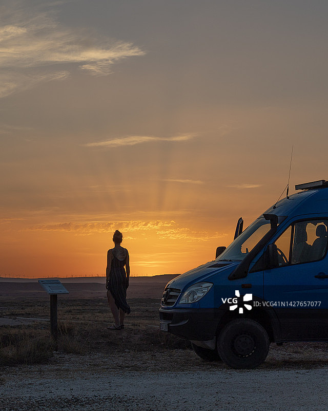 日落时分，一位孤独的年轻女子站在露营车旁图片素材