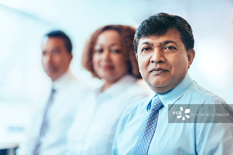 在明亮办公室里与同事共事的严肃成熟印度裔商人图片素材