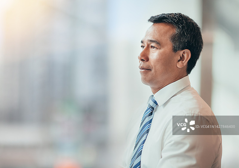 身穿商务装，在明亮办公室里沉思未来的亚洲成熟商人图片素材