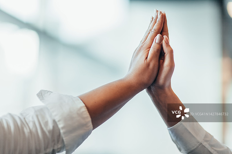 在明亮的商务办公室教室里，混血伙伴们叠手击掌，微笑庆祝达成协议、实现成功愿望图片素材