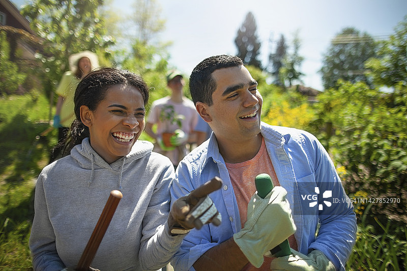 西班牙裔年轻女性和中东年轻男性学生在社区花园清理活动中微笑并展示成果图片素材