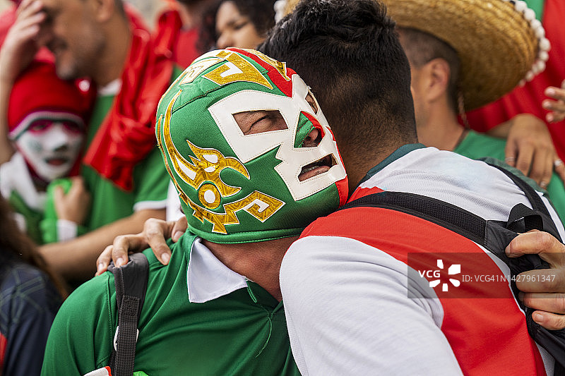 戴摔跤面具的墨西哥男子与朋友在足球比赛时拥抱图片素材