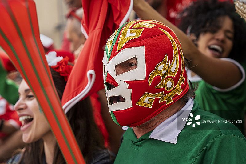 足球比赛中，戴着摔跤面具站在人群中的墨西哥男人图片素材