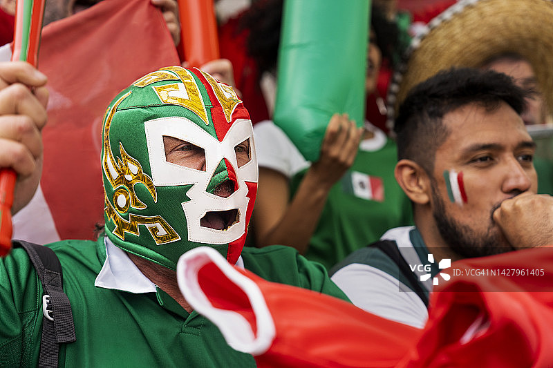 在体育场观看比赛时，戴着墨西哥摔跤面具的足球迷图片素材