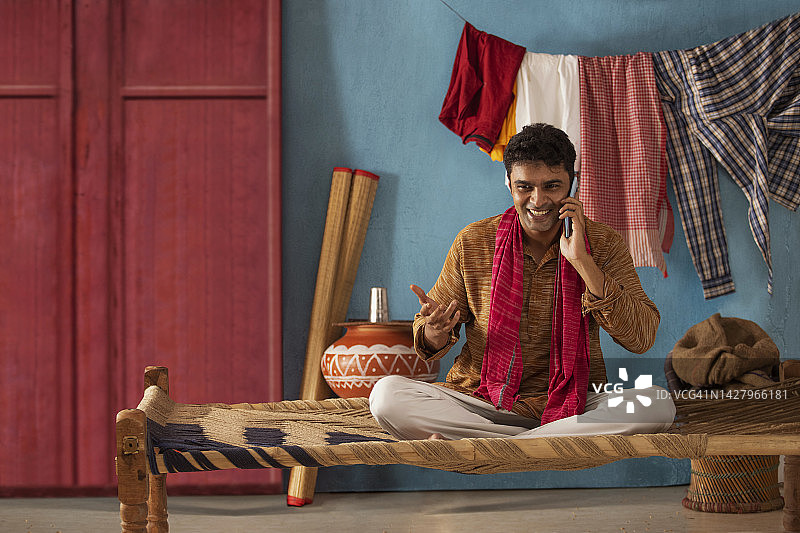 快乐的男人坐在小床上用手机聊天图片素材