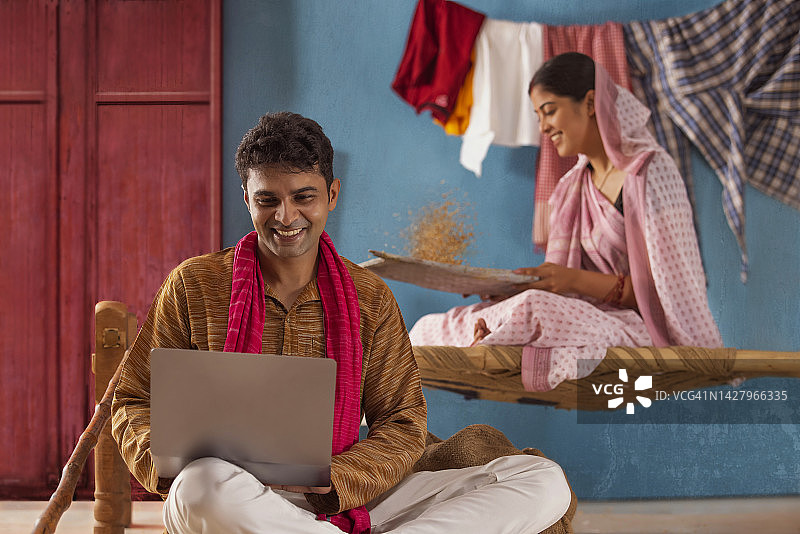 男人在家使用笔记本电脑，妻子在后面清理稻种图片素材