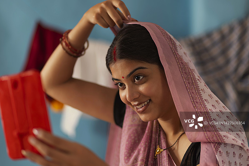 比哈尔邦妇女在手镜中看着自己并调整头巾的肖像图片素材