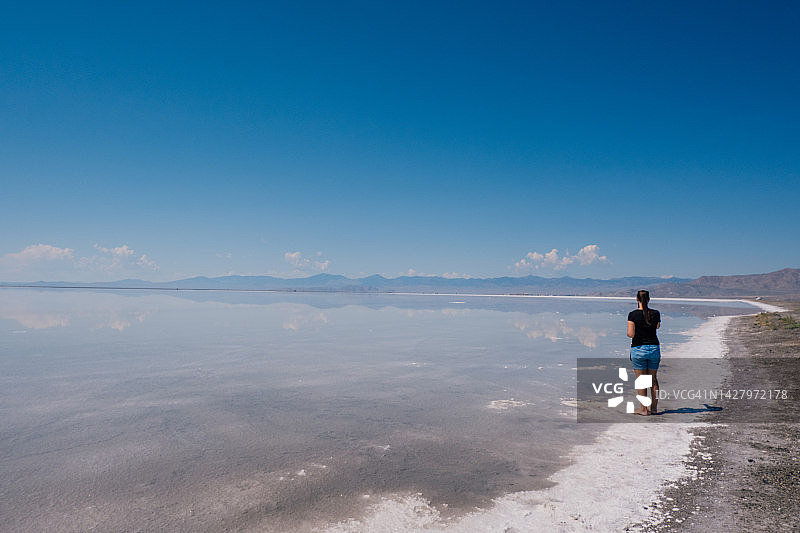 站在覆盖着水的博纳维尔盐滩上眺望远方的女人图片素材