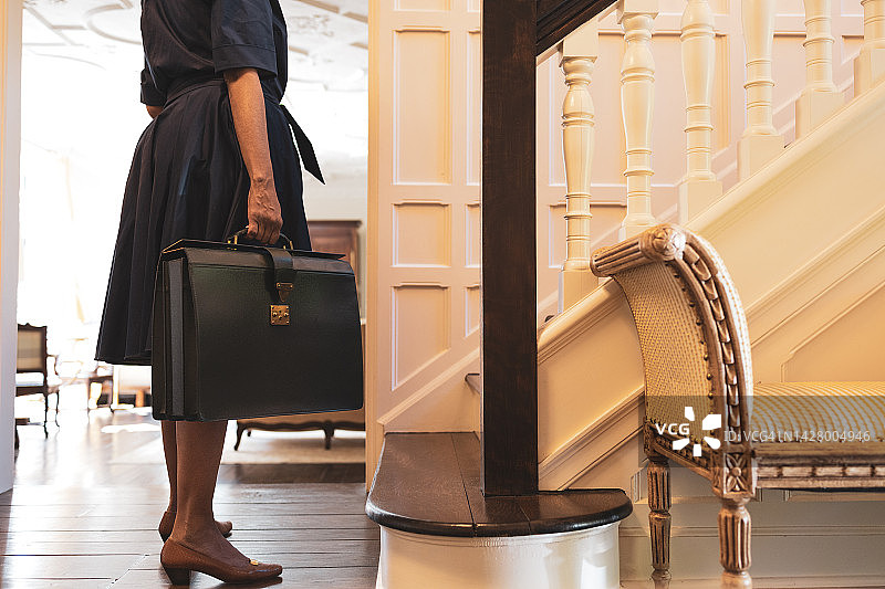 手提公文包、身穿喇叭裙和高跟鞋的黑人女性站在家中的门厅图片素材