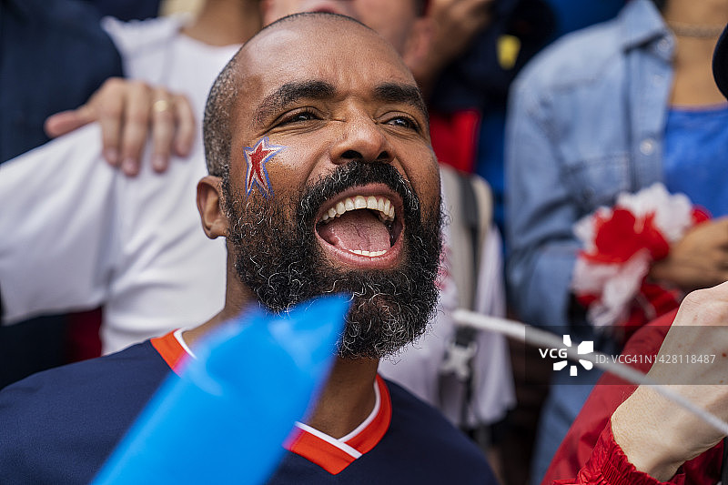 年轻男人脸上涂着油彩，在足球比赛中为国家队欢呼图片素材