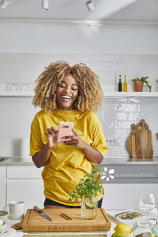 在厨房看手机微笑的年轻漂亮女人图片素材