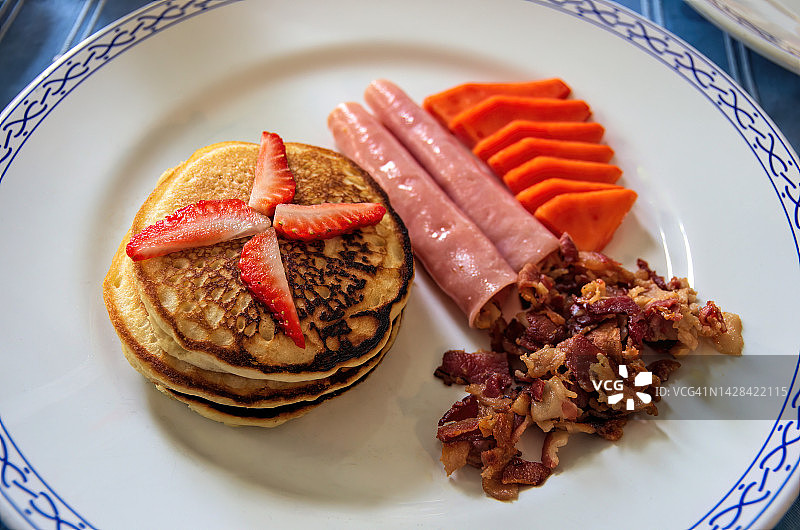 热香饼，顶部有切片草莓，配切片火腿、炸培根碎和切片木瓜图片素材