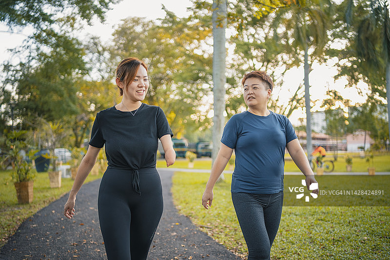 手臂畸形截肢的中国亚洲女性与朋友在公园日常傍晚跑步图片素材