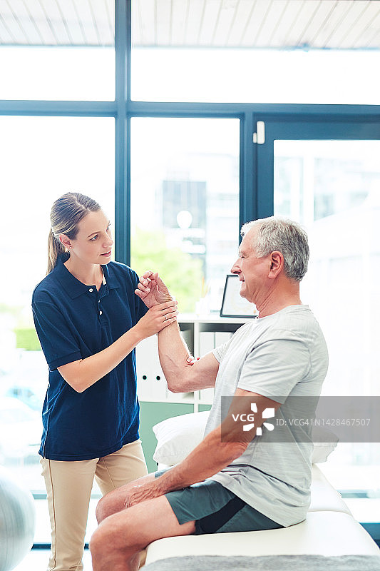 理疗师在诊所为患者进行按摩，帮助缓解手臂和手腕的疼痛、损伤或伤害。在办公室进行理疗，以放松身体的肌肉紧张或扭伤，为老年男性进行物理治疗图片素材