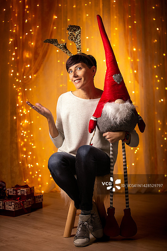 微笑的成年女性抱着坐在小凳子上的装饰精灵木偶图片素材