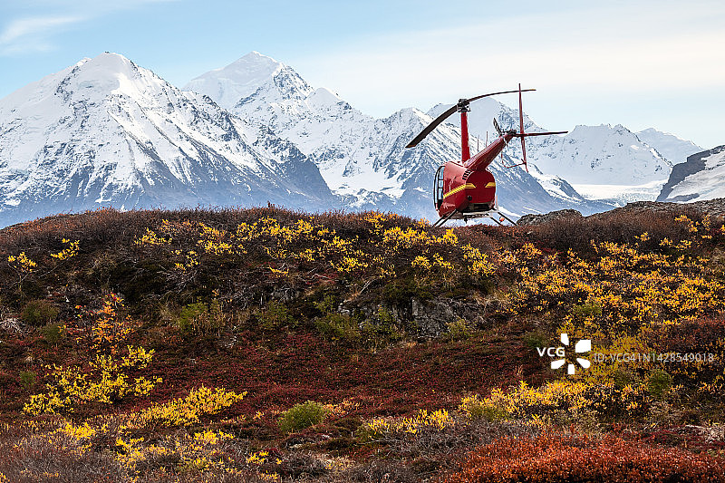 红色直升机掠过阿拉斯加克尼克冰川的秋色山脊图片素材