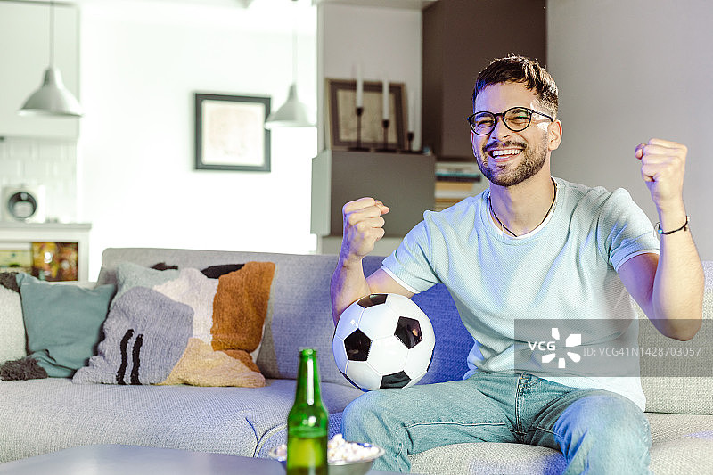 年轻男子坐在客厅里欢呼的照片图片素材