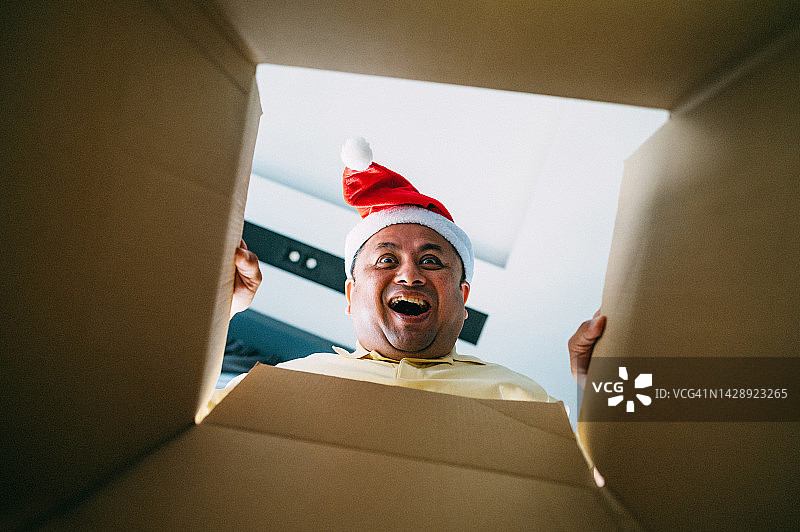 戴着圣诞帽，打开圣诞礼物的兴奋亚洲男人图片素材