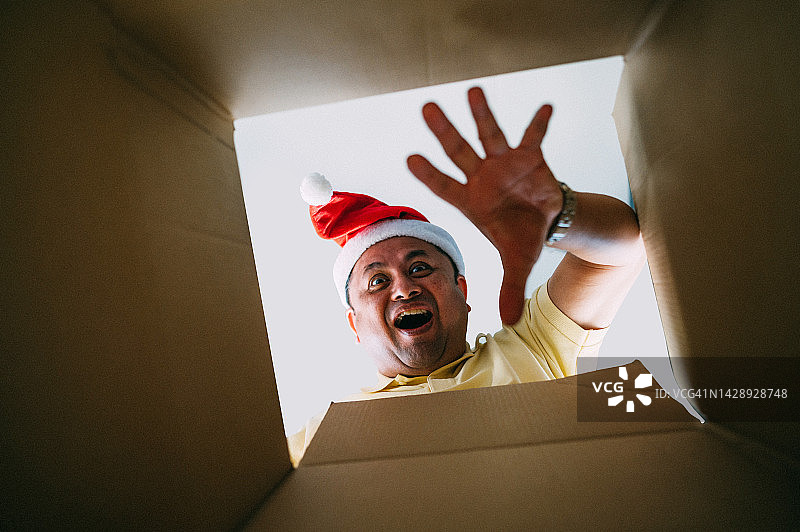 戴着圣诞帽，打开圣诞礼物的兴奋亚洲男人图片素材