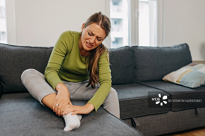 在沙发上，腿部疼痛的女人图片素材
