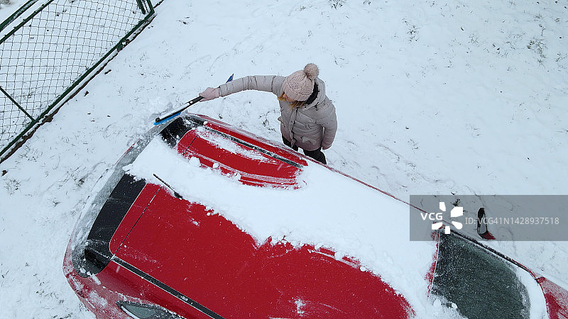 穿冬季夹克的女人正在刮车上的冰雪图片素材