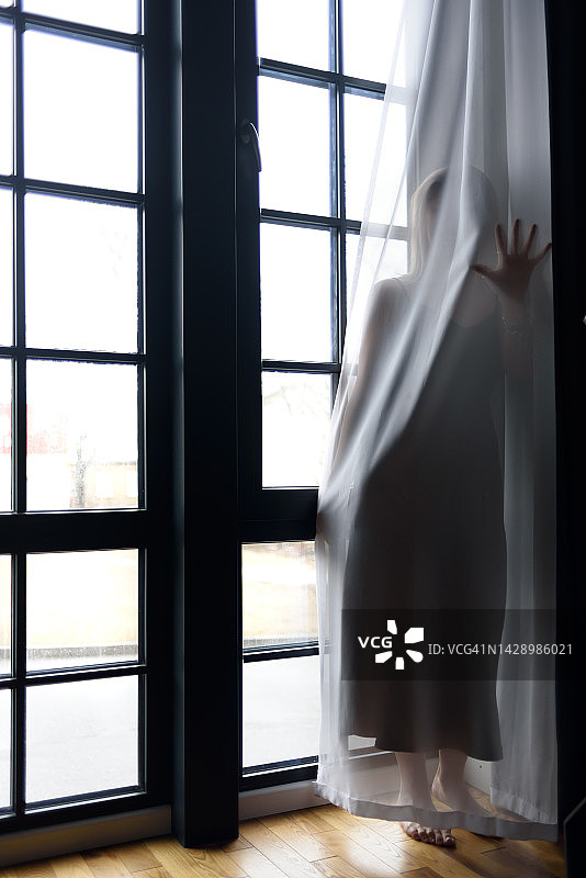 穿黑色连衣裙的女人站在窗帘后面图片素材