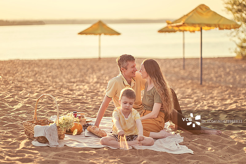 一家三口在海滩野餐，父母拥抱在一起图片素材