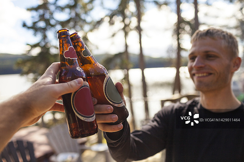 两个男人在湖边周末旅行时用啤酒瓶敬酒图片素材