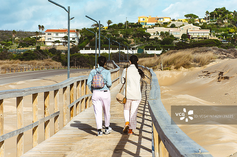姐妹在海滩木栈道上行走的背影图片素材