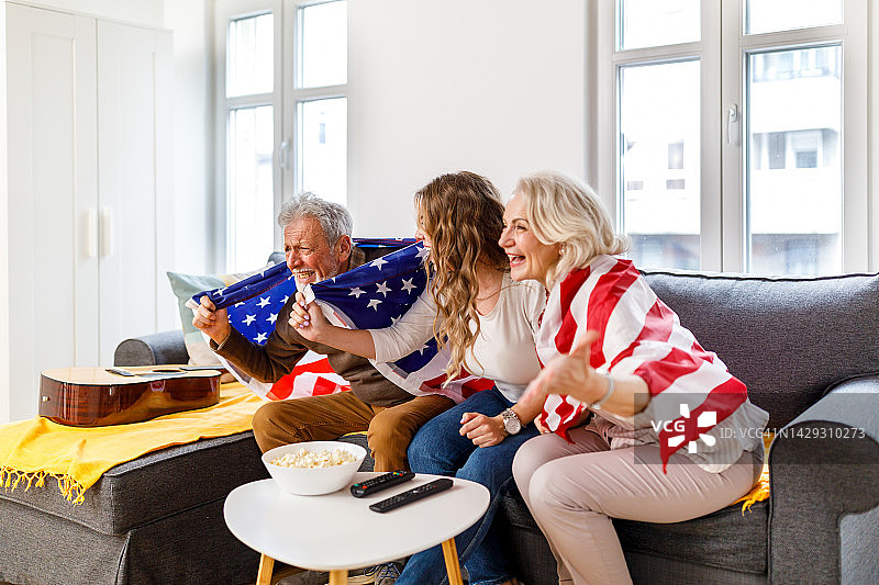 年轻女子和祖父母在舒适的公寓里观看体育比赛，支持美国队图片素材