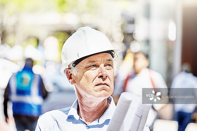 建筑师、土木工程师或建筑主管拿着图纸走在街上，戴着白色安全帽图片素材