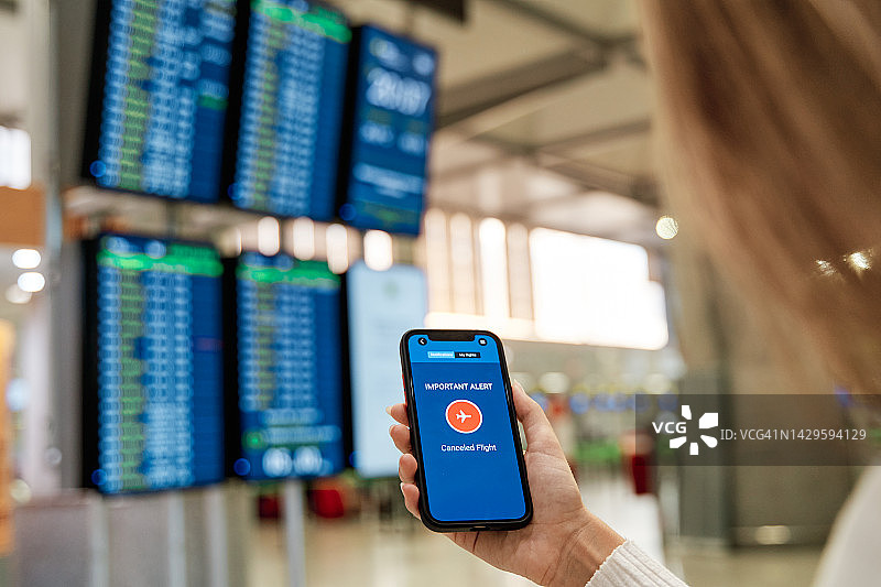 机场航站楼内手持手机接收航班取消通知的女子手部特写图片素材