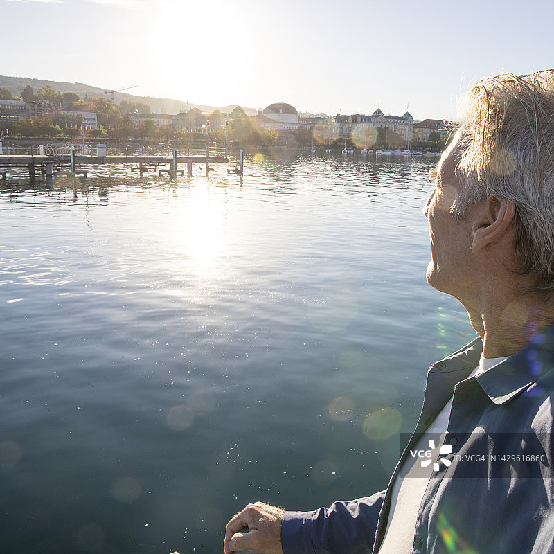 成熟男人观看湖面和城市日出的侧面照图片素材