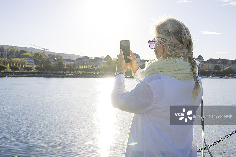 日出时分，中年妇女在湖岸边使用手机图片素材