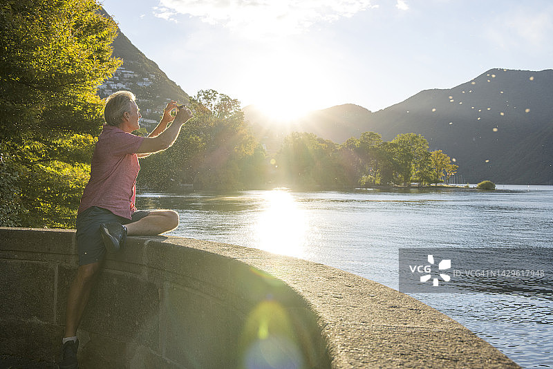 日出时分在湖岸边使用手机的中年男人图片素材
