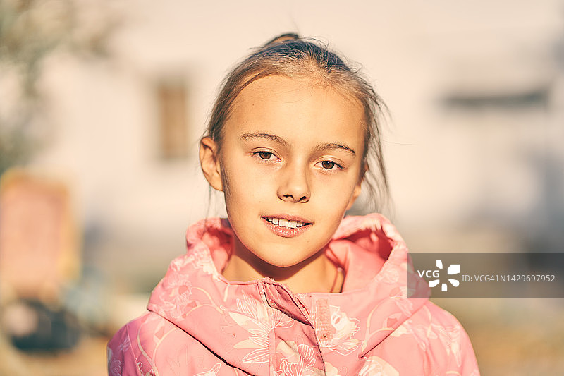 穿着粉色运动衫的漂亮女孩站在户外，微笑直视镜头，一个快乐的8岁儿童，快乐童年图片素材