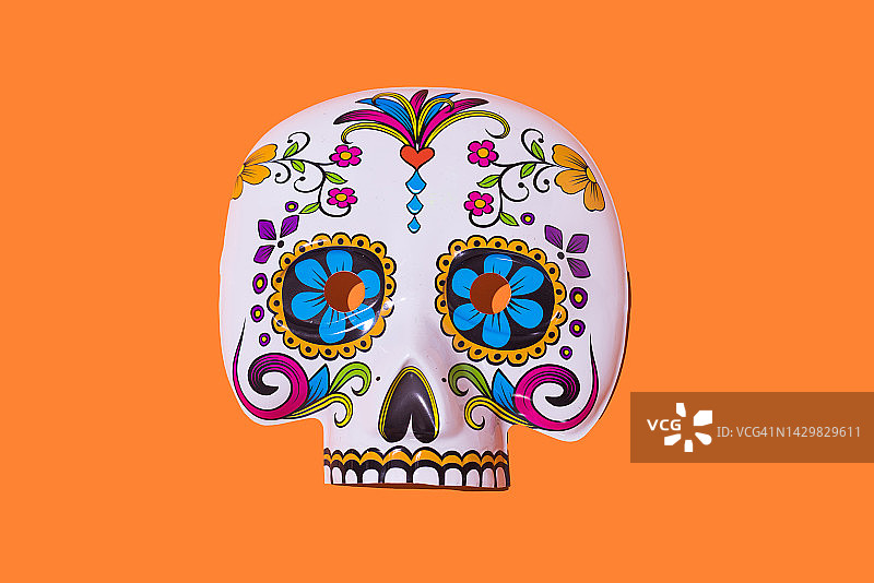 橙色背景上的白色和彩色骷髅面具，源于墨西哥亡灵节，万圣节、亡灵节、庆祝活动、服装和精神概念图片素材