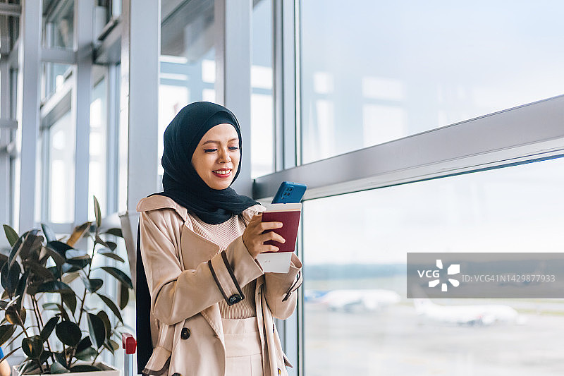 拿着护照和登机牌，正在使用智能手机的穆斯林妇女图片素材