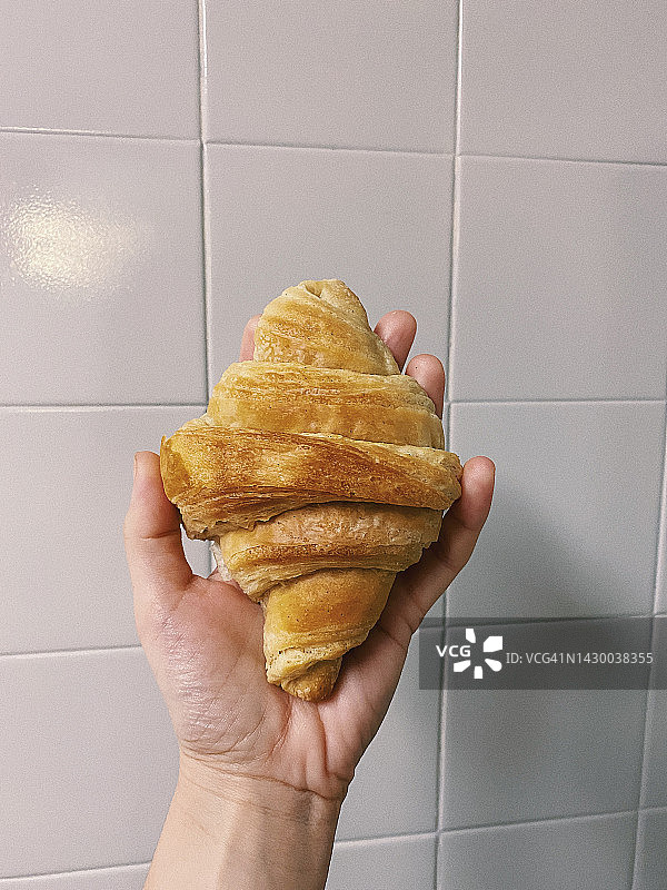 女性左手拿着的自制牛角面包，正面视图，使用Iphone 11拍摄。图片素材